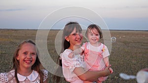 Happy mother playing with children blowing soap bubbles. children catch bubbles and laugh in the park in summer. Slow