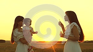 Happy mother playing with children blowing soap bubbles. Daughters and mother are blowing bubbles in the park at sunset