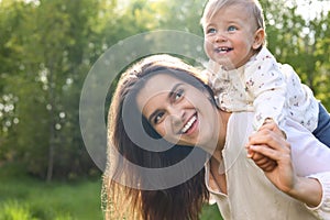 Happy mother playing with her cute baby in park on sunny day, space for text