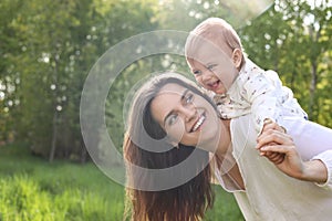 Happy mother playing with her cute baby in park on sunny day, space for text