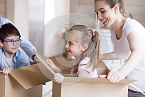 Happy mother playing with kids unpacking boxes at new house