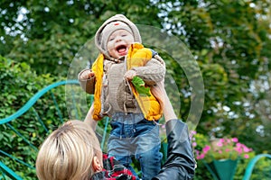 Happy mother playing with a small son, throwing in the air, outdoors in autumn park. Mom throws her little smiling baby