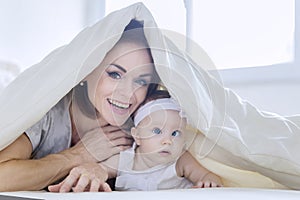 Happy mother plays with her baby under a blanket