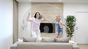Happy mother and preteen daughter jumping on sofa together, baby sitter or mother playing having fun with cute kid girl