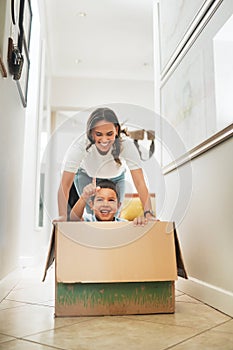 Happy mother pushing son in cardboard box enjoying their new home.Little boy having fun riding in carton box