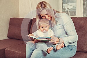 Happy mother read a book to child girl indoors sitting on couch