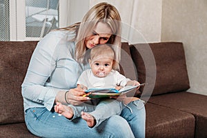 Happy mother read a book to child girl indoors sitting on couch