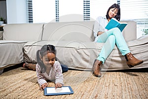 Happy mother reading book while her daughter using tablet