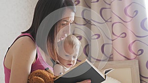 Happy mother reading a book to child boy indoors. Sweet moment with mother reading book to baby.