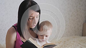 Happy mother reading a book to child boy indoors. Sweet moment with mother reading book to baby.