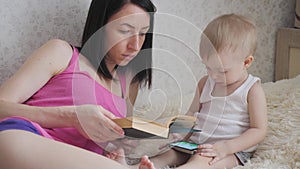 Happy mother reading a book to child boy indoors. Sweet moment with mother reading book to baby.