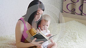 Happy mother reading a book to child boy indoors. Sweet moment with mother reading book to baby.