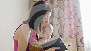 Happy mother reading a book to child boy indoors. Sweet moment with mother reading book to baby.