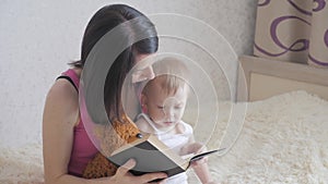 Happy mother reading a book to child boy indoors. Sweet moment with mother reading book to baby.