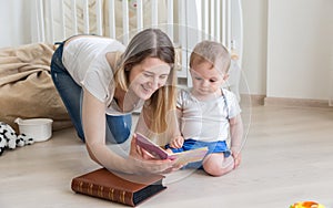 Happy mother reading book to her 10 months old baby boy on floor
