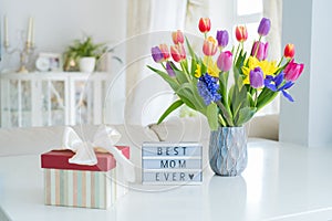 Happy Mother`s Day background. Colorful spring flowers bouquet in vase, gift box with satin ribbon and lightbox with words Best