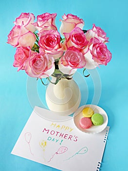 Happy mother`s day with beautiful bouquet of pink roses and tulips, french macaroni and card on blue background, spring flowers