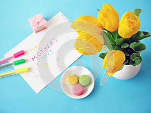 Happy mother`s day with beautiful bouquet of pink roses and tulips, french macaroni and card on blue background, spring flowers