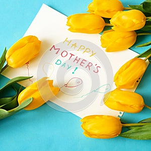 Happy mother`s day with beautiful bouquet of yellow and red tulips and card on green background, spring flowers flat lay