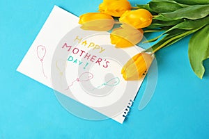 Happy mother`s day with beautiful bouquet of yellow and red tulips and card on green background, spring flowers flat lay