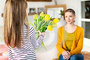 Happy Mother`s Day or Birthday Background. Adorable young girl surprising her mom with bouquet of yellow tulips.