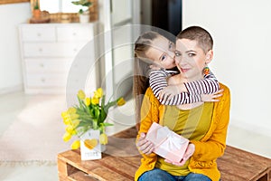 Happy Mother`s Day or Birthday Background. Adorable young girl surprising her mom, young cancer patient, with bouquet and present.