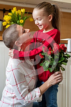 Happy Mother`s Day or Birthday Background. Adorable young girl surprising her mom, young cancer patient, with bouquet of red roses