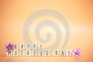 Happy Mother's Day Card. Text Happy mothers Day on bright pastel orange colored background with colorful purple flowers,