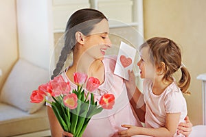 Happy Mother`s Day. The child daughter congratulates her mother and gives her a homemade card and flowers pink tulips