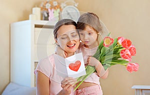 Happy Mother`s Day. The child daughter congratulates her mother and gives her a homemade card and flowers pink tulips