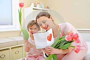 Happy Mother`s Day. The child daughter congratulates her mother and gives her a homemade card and flowers pink tulips