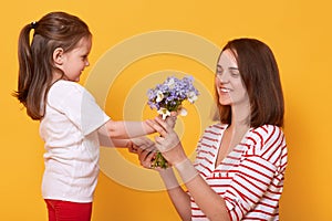 Happy mother`s day! Child daughter congratulates mom and gives her bouquet of flowers. Mum wearing striped shirt and little girl