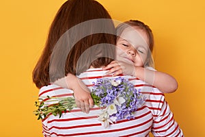 Happy Mother`s day! Child daughter congratulates mom and gives her flowers. Mum and little girl hugging, charming kid closes eyes