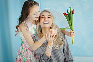 Happy mother`s day. Child daughter congratulates moms and gives her a postcard and flowers tulips.