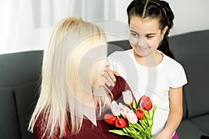 Happy mother's day. Child daughter congratulates moms and gives her a postcard and flowers tulips