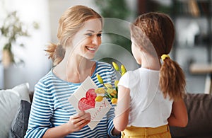 Happy mother`s day! Child daughter congratulates moms and gives her a postcard and yellow flowers tulip