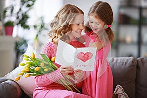 Happy mother`s day! child daughter gives mother a bouquet of flowers to tulips and postcard