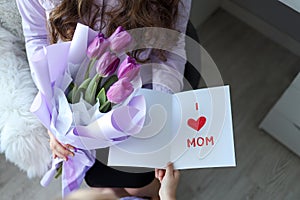 Happy mother`s day! The child`s daughter congratulates her mother and gives her flowers tulips and a postcard: I love you, mom