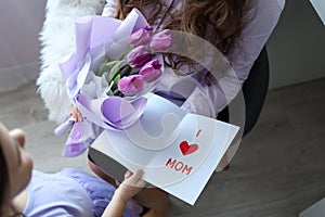 Happy mother`s day! The child`s daughter congratulates her mother and gives her flowers tulips and a postcard: I love you, mom