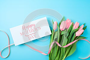 Happy Mother`s day concept with greeting card and beautiful tulip flowers on blue background. Flat lay, top view