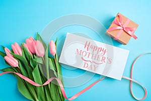 Happy Mother`s day concept with greeting card, gift box and beautiful tulip flowers on blue background. Flat lay, top view