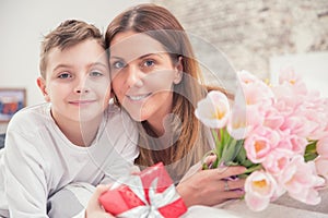 Happy mother`s day concept. Mom with son on bed with gift and tulips