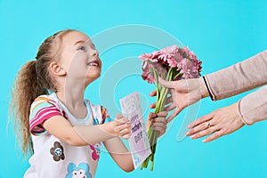 Happy Mother`s Day. Cute little girl giving mom greeting card and bouquet of pink gerbera daisies. Mother and daughter concept.