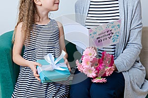 Happy Mother`s Day. Cute little girl giving mom greeting card, present and bouquet of pink gerbera daisies. Mother and daughter.