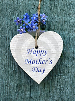 Happy Mother`s Day greeting card with decorative white heart and forget-me-not flowers on old blue wooden background.