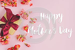 Happy mother`s day greeting card. Happy mothers day text and gift box with red flowers on pink background flat lay. Stylish flora