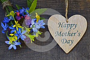 Happy Mother`s Day greeting card with spring flowers bouquet and decorative heart on old wooden background.