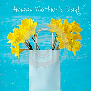 Happy mother`s day greeting card. Spring yellow daffodils in a gift bag on a turquoise background