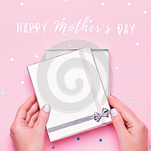 Happy Mother`s Day greeting card with woman opening silver gift box on pink background with confetti. Giving presents for Mother