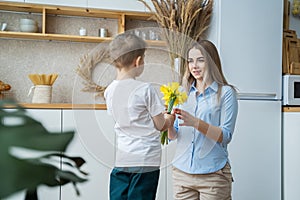 Happy mother`s day! little son gives flowers to mom; boy congratulates mom; flowers in the hands of a boy; yellow daffodils; happy